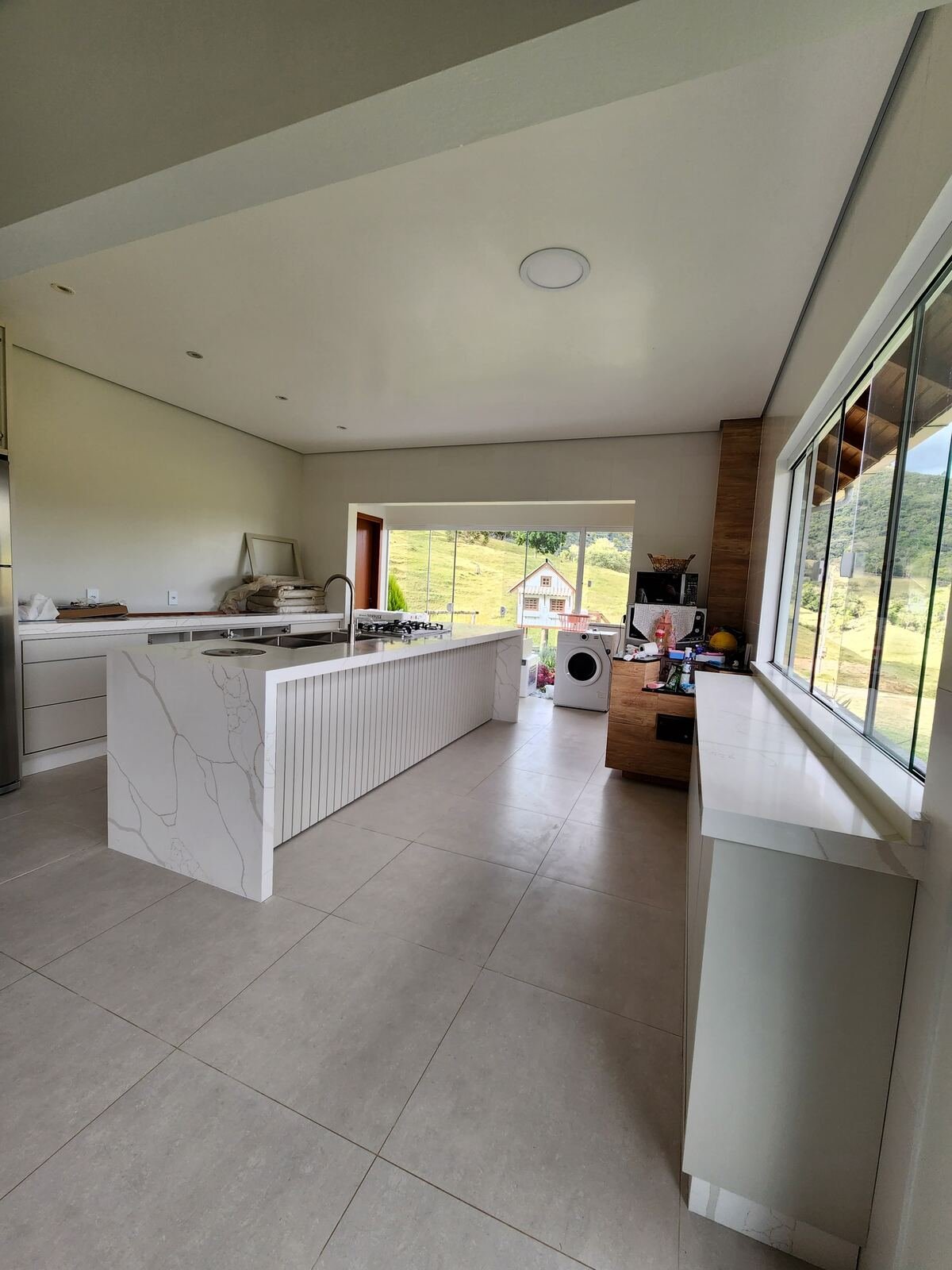 Cozinha ampla com ilha em quartzo branco e vista para o campo