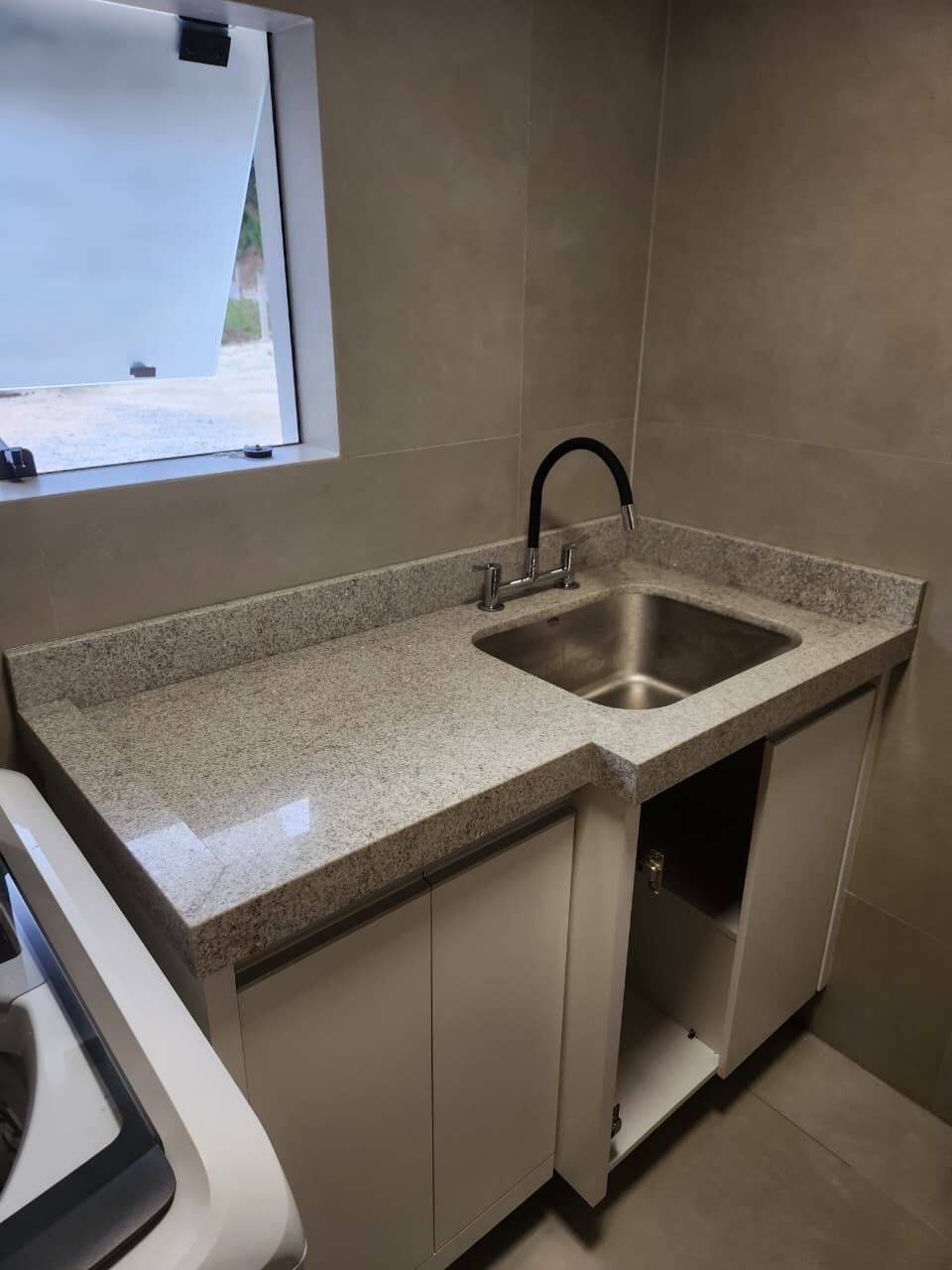 Bancada de granito bege com cuba de inox em área de serviço